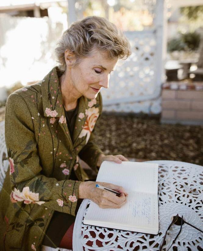 Photo of a senior lady sitting in a garden at a table writing in a journal.